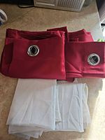 two folded red grommet-top panels stacked with two folded white sheers