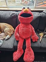 Front view of oversized red Elmo plush seated on couch