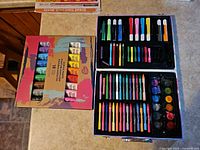 Acrylic paint set beside open art supply case showing contents