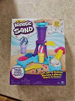 Front of sealed Kinetic Sand Soft Serve Station box showing contents and 14 oz weight