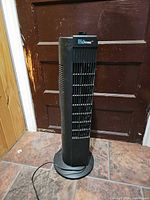 Full view of black Living tower fan standing on base with cord visible