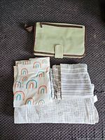 Folded green Munchkin changing pad organizer with three muslin covers laid beneath