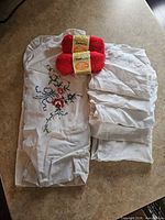 Group shot of two red yarn skeins and five white linen pieces