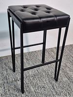 Full view of metal stool showing legs and tufted seat
