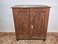 Front view of antique wooden cabinet showing two arched panel doors, lock, bun feet