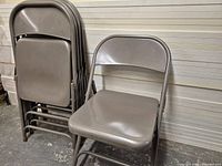 Five gray metal folding chairs stacked and one open
