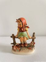 Front view of figurine showing girl on fence, basket and flowers