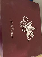 Maroon lid with The Danbury Mint logo and holly bow design