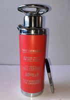 Front view of red “Thirst Extinguisher” decanter with chrome pump top next to Sharpie for scale