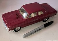 Left side view of burgundy 1964 Ford Fairlane diecast with marker for scale