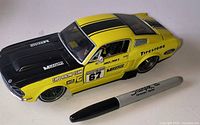 Driver side view of yellow/black Ford Mustang diecast car showing #67, decals, wheel detail