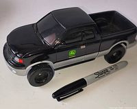 Left front side view of black John Deere diecast pickup beside Sharpie for scale