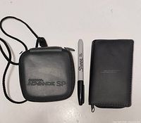 Front view of closed Game Boy Advance SP case beside closed Bose case and Sharpie for scale