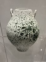 Front view of white ceramic vase with green splatter pattern and two loop handles