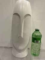 Front view of white abstract face vase beside bottle for scale