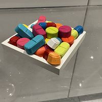 Top angled view of sculpture showing colorful pill forms on white square base