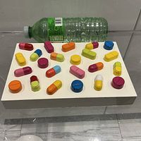 Angled view showing entire pill sculpture on white base with bottle for scale