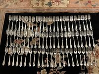 Overhead view of 72 matching forks arranged in rows on rug