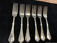 Six matching dinner forks aligned on black background