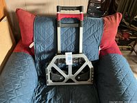 Folding hand truck collapsed on chair, showing front view of base plate and telescoping handle