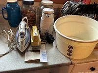 All items grouped on countertop: steam iron, fabric shaver, coffee carafe, wash basin, glass jars, mug, adapter