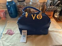 Front view of blue croc-embossed handbag with VO charm