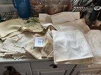 Overall lot showing napkins, embroidered hankies, crocheted doilies on countertop