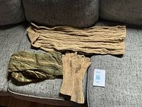 Overall view of tan knit scarf, tan gloves, green shawl on sofa