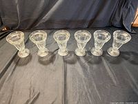 Six of the clear ribbed footed glasses lined up rim to rim