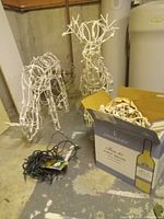 Two white wire reindeer frames, loose string lights, cardboard box