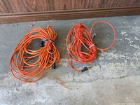 Both coiled orange extension cords on floor