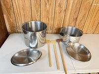 Both stock pots, two lids, three wooden spoons displayed on table
