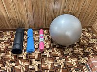 Three rolled yoga mats and one inflated silver stability ball on patterned floor