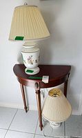 Demilune wood table with two ceramic floral lamps, one lamp on top, one on floor beside