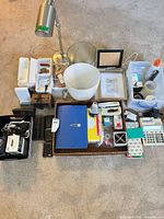 All items grouped on floor: lamp, frames, organizers, electronics, tray, binder, wastebasket, calculator, cables