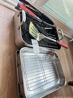 Overall view of two roasting pans, wire rack, utensils and measuring cup