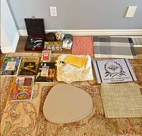 Overview of lot items laid out on floor showing books, wine tool set, coasters, votive holder, napkin rings, linens and placemats