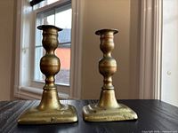 Front view of both brass candlesticks showing overall form and patina