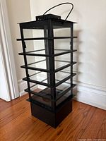 Front view of black metal and glass lantern showing slat design, glass panes, handle, base