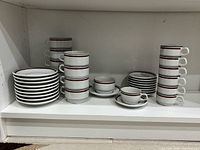 Full set of stacked cups and saucers on shelf showing quantity and design