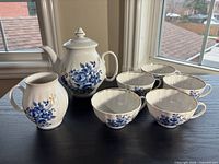 Full tea set on tabletop: teapot with lid, creamer, five cups