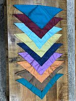 Stacked view of nine coloured silk pocket squares fanned to show colours