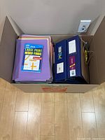 Box showing coloured paper, puzzle book, two binders