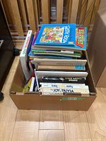 Box of assorted books showing children’s, trivia and instruction titles