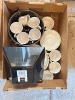 Dinnerware and mugs stacked inside box with Bundt pan and black bowl visible