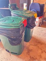 Two green wheeled trash carts with lids and latches