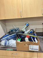 Box containing hockey stick, skates, gloves, mesh net, tape rolls, accessories