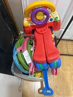 Top view of red/yellow ride-on toy with steering panel and blue handle, green fabric tunnel beneath