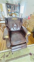 Front view showing brown leather wingback recliner with rolled arms, nailhead trim and extended footrest