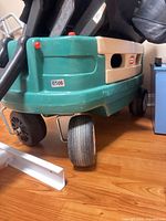 Front corner view showing teal body, beige side rail, worn front wheel